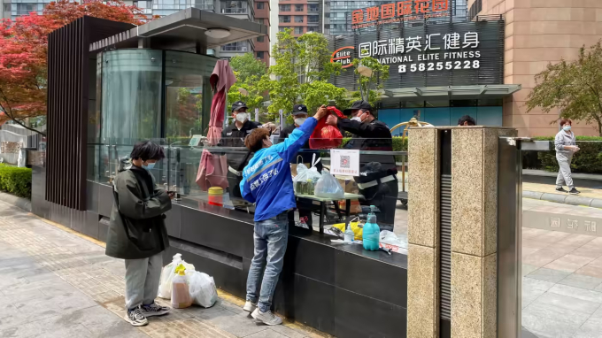 Một người chuyển phát nhanh giao lệnh giao hàng cho một nhân viên bảo vệ qua hàng rào khi Bắc Kinh phong tỏa các khu dân cư trong bối cảnh COVID-19 bùng phát. Ảnh: Reuters