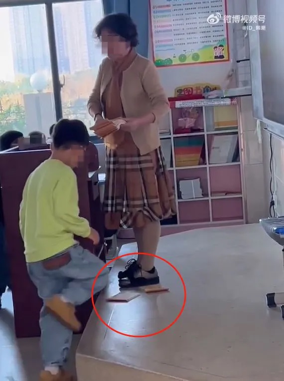 Trong đoạn video, cô giáo tóc ngắn gọi tên và giao bài tập cho học sinh nhưng thay vì trực tiếp đưa cho các em, cô lại liên tục ném dưới chân.