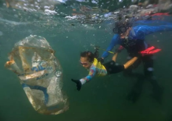 Bức ảnh ghi lại hình bé Nina Gomes, 4 tuổi, cùng với cha là nhà sinh vật biển, dọn rác thải nhựa tại bãi biển Praia Vermelha ở Rio de Janeiro, Brazil hồi tháng 7/2021. Cô bé Nina Gomes đã trở thành “Đặc vụ Xanh” trẻ tuổi nhất của Công ty Vệ sinh đô thị tại thành phố Rio de Janeiro, Brazil vì những nỗ lực thu gom rác thải trên biển của mình. Ảnh: Reuters