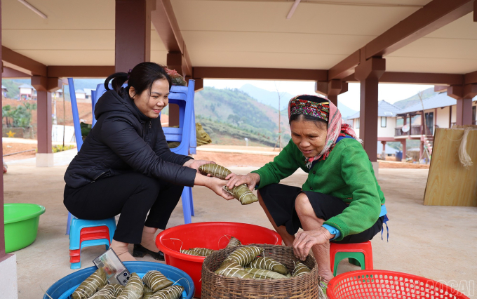 Chị Vũ Thị Tư (bên trái), Bí thư Đảng ủy xã Phúc Khánh đến thăm, động viên các hộ dân ở khu tái định cư Làng Nủ. Bà Hoàng Thị Nóng (bên phải) vui vẻ giới thiệu chiếc bánh chưng gù truyền thống của người Tày nơi đây. Ảnh: baolaicai.vn