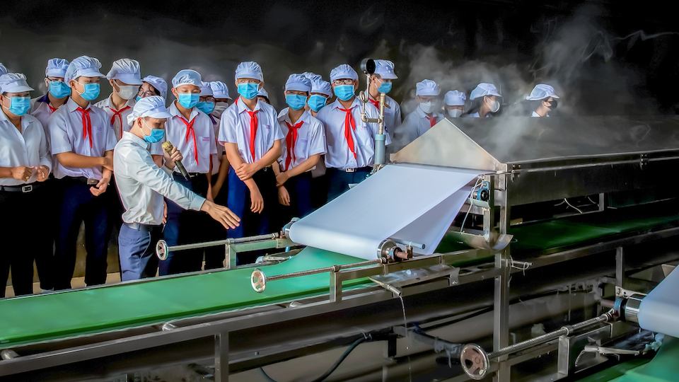 Các em học sinh tìm hiểu quy trình tráng bánh tráng bằng công nghệ hiện đại trong chuyến tham quan, trải nghiệm thực tế tại nhà máy Tân Nhiên (Tây Ninh)