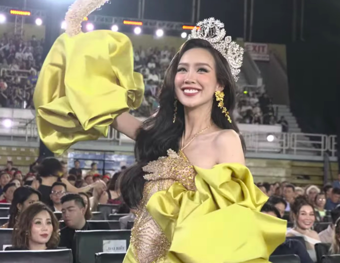 Bảo Ngọc diện đầm vàng, đội vương miện Miss Intercontinental, vẫy tay chào khán giả khi tên cô được xướng lên