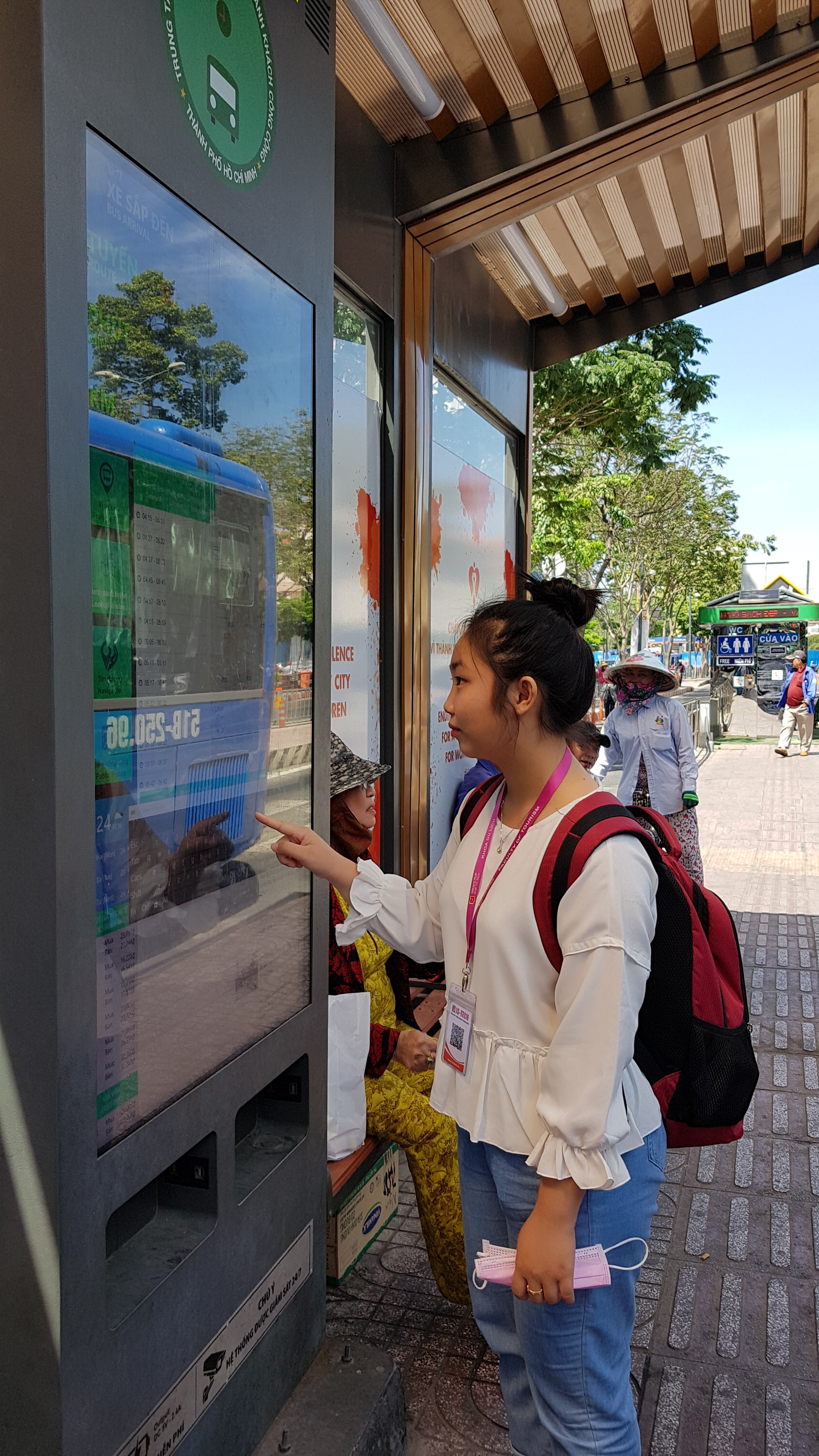 Một ban trẻ đọc báo, xem thông tin chuyến xe ngay trạm chờ xe buýt, công nghệ số đã đi vào cuộc sống hằng ngày của người dân  - Ảnh: Cẩm Viên 