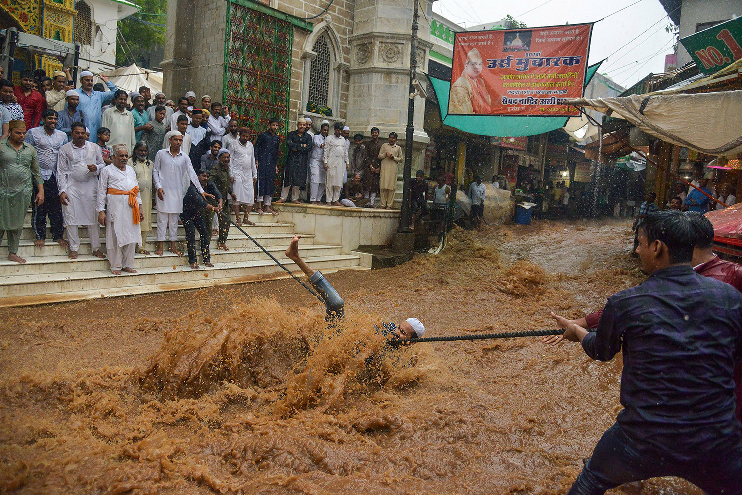 Một người đàn ông đi trong dòng nước lũ ào ạt khi anh ta cố gắng giữ một sợi dây để giúp mọi người băng qua đường sau những cơn mưa gió mùa nặng nề bên ngoài đền thờ Moinuddin Chishti Sufi ở Ajmer, Ấn Độ, vào ngày 1/8.