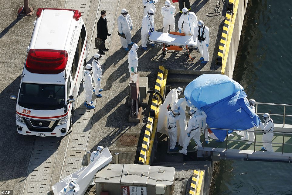 Nhân viên y tế trong bộ đồ bảo hộ dẫn một hành khách được xét nghiệm dương tính với một loại coronavirus mới từ tàu du lịch Diamond Princess tại cảng Yokohama. Ảnh: AP.