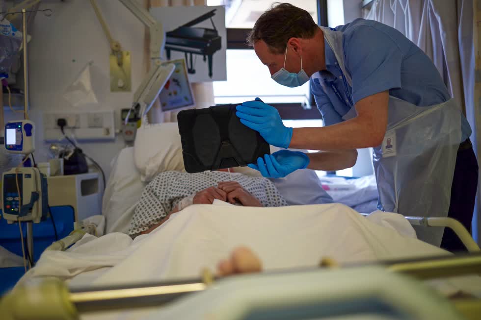 Một y tá giúp một bệnh nhân giao tiếp với gia đình qua ứng dụng Zoom tại một bệnh viện ở Blackburn, Anh, vào ngày 14/5. Vào tháng 12, Vương quốc Anh trở thành quốc gia phương Tây đầu tiên cho phép tiêm chủng COVID-19. Ảnh: Reuters / Bloomberg