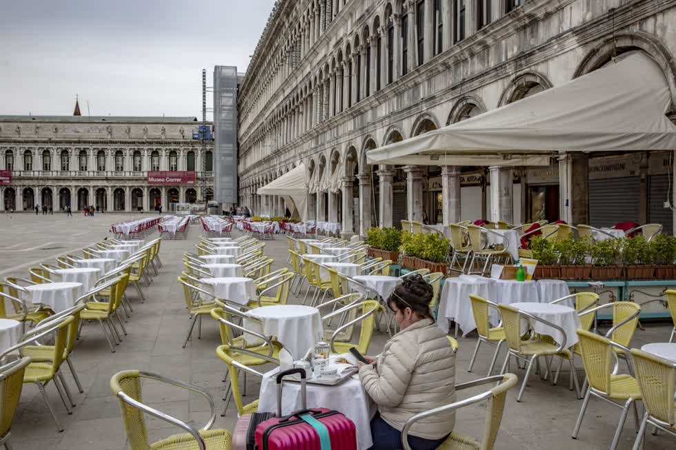   Một quán ăn ở Piazza San Marco của Venice vào ngày 5/3. Khi đại dịch tăng nhanh trong năm, ngành khách sạn và thực phẩm đã phải chịu những tổn thất tài chính đáng kể, (ảnh trái). Những người tham dự triển lãm Caravan Salon ở Düsseldorf, Đức, kiểm tra một ngôi nhà mô hình sang trọng vào ngày 8/9. Các loại xe giải trí đã chứng kiến ​​sự gia tăng đáng kể trong doanh số bán hàng trong năm nay do mọi người tìm cách đi xa trong khi tránh xa đám đông. Ảnh: Bloomberg  