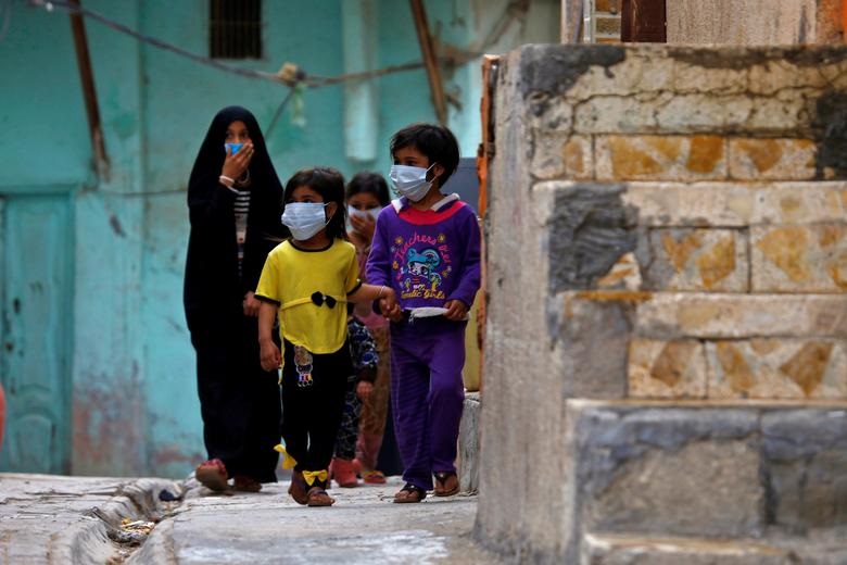   Trẻ em Iraq đeo khẩu trang bảo vệ khi chúng đi bộ gần một trường tôn giáo, nơi phát hiện trường hợp nhiễm COVID-19 đầu tiên, sau khi dịch COVID-19 bùng phát, tại thành phố thánh Najaf, Iraq, ngày 24/2.   