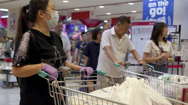   Một người phụ nữ đeo khẩu trang và găng tay đẩy xe hàng tạp hóa của mình ra khỏi siêu thị sau khi tin virus corona bùng phát, người dân đã hoảng loạn dự trữ nhu yếu phẩm vào ngày 9/2 tại Singapore. Ảnh CNBC.  