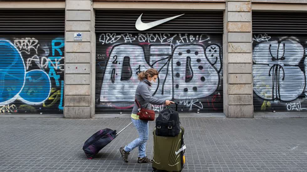   Một khách du lịch đeo mặt nạ bảo vệ khi cô xách vali qua cửa hàng Nike đã đóng cửa tại Las Ramblas, ngày 15/3/2020, tại Barcelona, ​​Tây Ban Nha.  