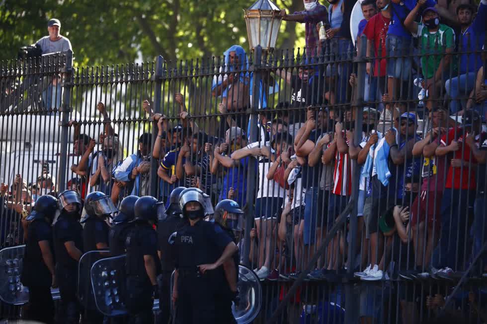 Những người hâm mộ đưa tang trèo lên hàng rào của dinh tổng thống để nhìn thoáng qua chiếc quan tài chở thi hài của Diego Maradona.