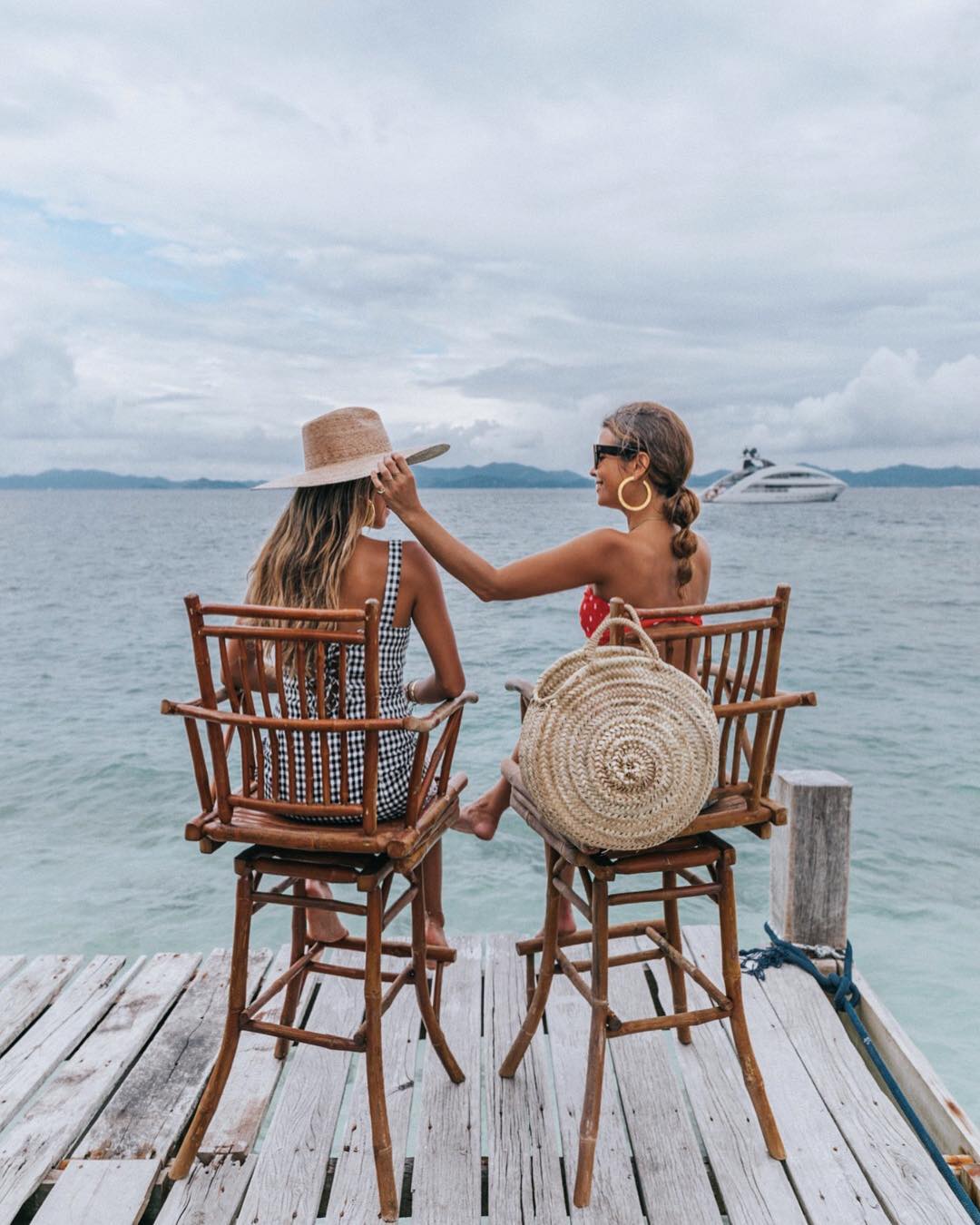 Hai cô gái ngồi ngoài biển, xách túi cói đi biển