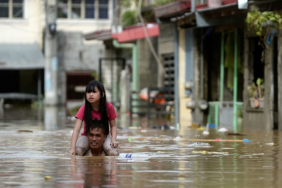Một người đàn ông cõng một đứa trẻ trên vai khi anh ta lội qua một con đường ngập lụt ở tỉnh Rizal. Ảnh: Reuters