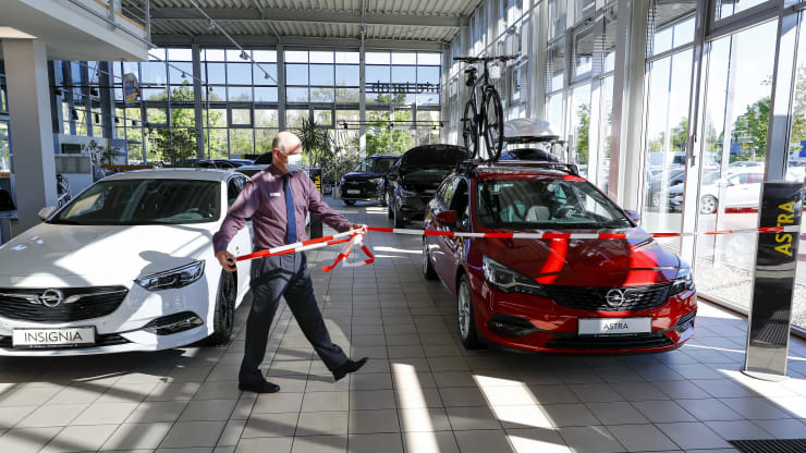 Một nhân viên đeo khẩu trang bảo vệ đã gỡ bỏ một sợi dây bên cạnh ô tô Opel Insignia và Opel Astra, do Adam Opel AG sản xuất, khi các nước Đức bắt dỡ bỏ lệnh phong toả  theo từng giai đoạn của một số doanh nghiệp. Ảnh: Bloomberg.