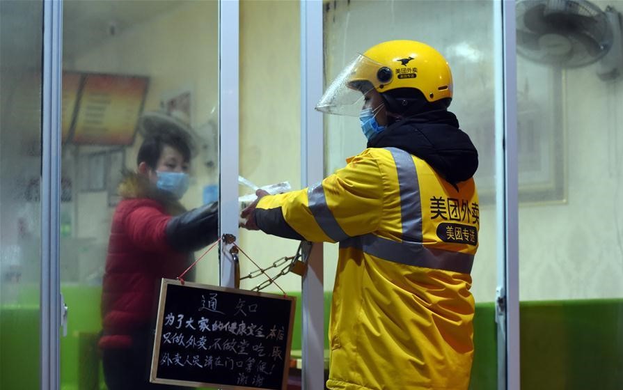 Một nhân viên giao hàng của Meituan cẩn thận đưa thức ăn qua những cánh cửa bị xích vì cách ly trong đại dịch. Ảnh: Xinhua