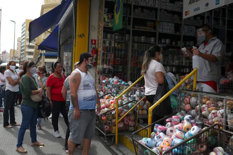 Nhân viên kiểm tra nhiệt độ của một người phụ nữ khi mọi người xếp hàng để vào cửa hàng tại Sao Paulo,  Brazil . Ảnh: Reuters.