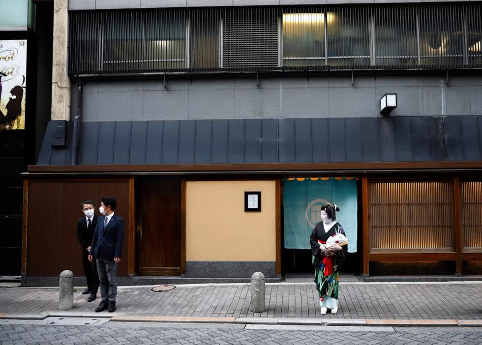  Nhân viên nhà hàng đeo khẩu trang bảo vệ khi họ đứng trên đường với Ikuko khi họ chờ một geisha khác đến bên ngoài nhà hàng Asada.