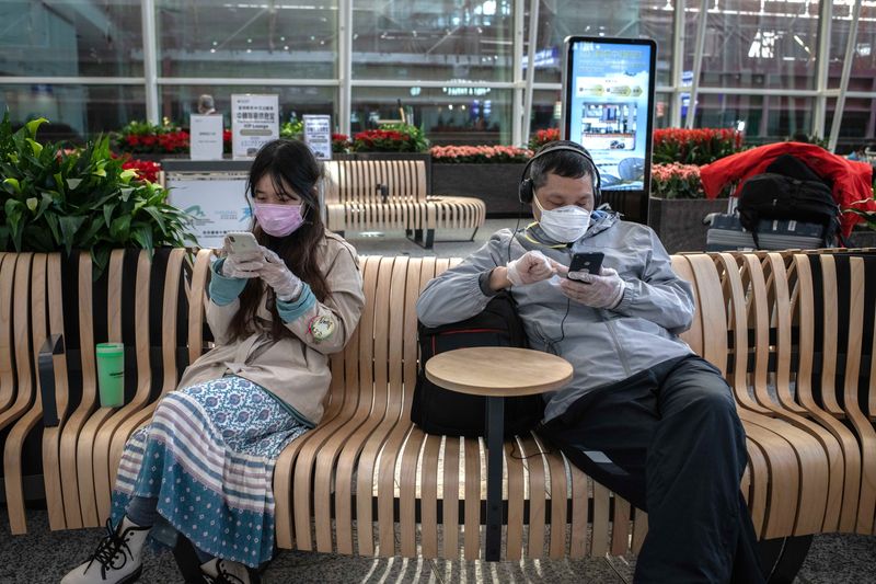 Hành khách đeo khẩu trang và găng tay khi sử dụng điện thoại thông minh tại Sân bay Quốc tế Hồng Kông. Ảnh: Bloomberg