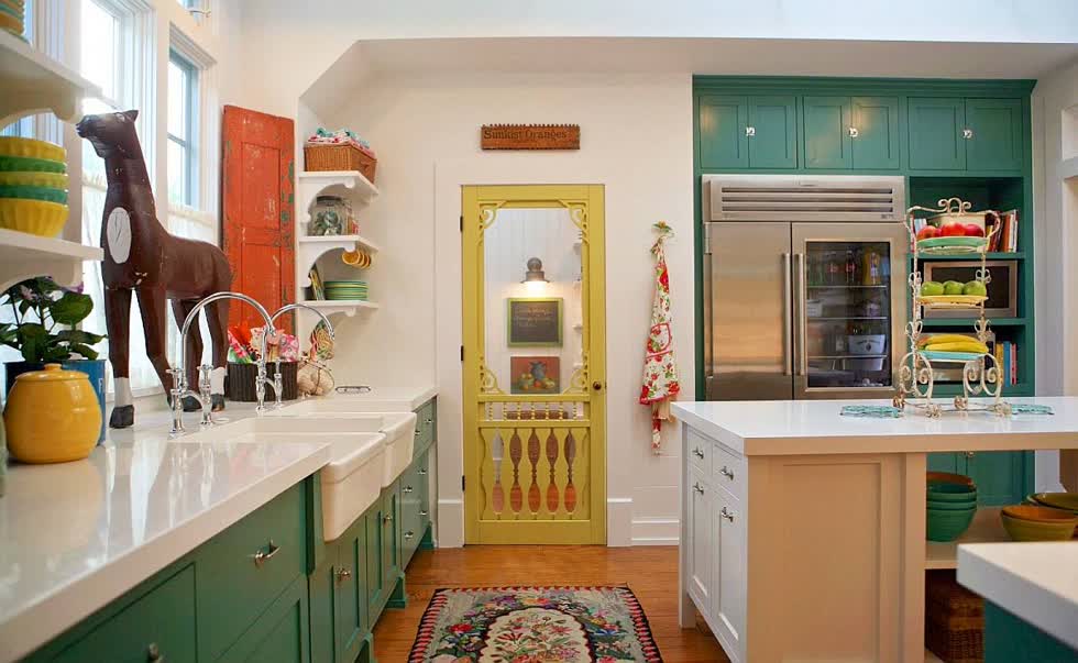   Nhà bếp phong cách nông trại nổi bật với tủ màu xanh lá cây, một cánh cửa màu vàng và sắc cam đất tạo điểm nhấn.  