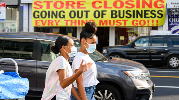   Những người đi bộ đeo khẩu trang đi ngang qua một tấm biển được treo bên ngoài một cửa hàng bán lẻ ở Harlem, thành phố New York, nói rằng họ sắp ngừng hoạt động. Ảnh: Getty Images.  