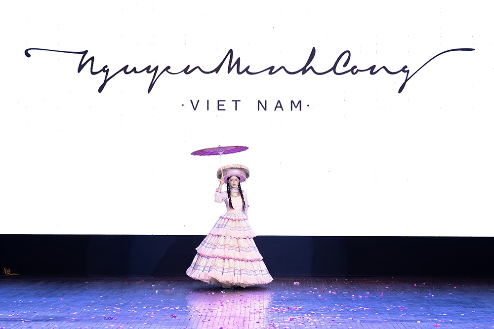 Chiếc ô trở thành một phần của màn trình diễn, trong khi họa tiết thổ cẩm được đưa vào trang phục như một chất liệu kể chuyện. Cách xử lý này giúp những yếu tố truyền thống hiện diện tự nhiên, không tạo cảm giác nặng tính minh họa hay phục dựng.