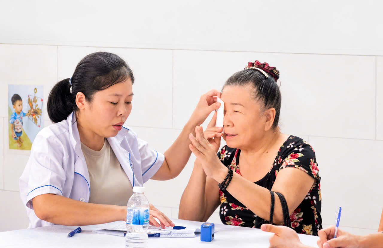 Nũ cán bộ y tế cơ sở khám mắt cho phụ nữ địa phương