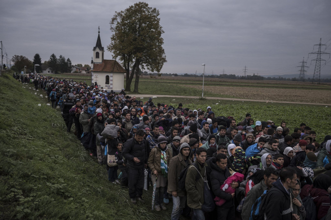 Ngày 22 tháng 10 năm 2015. Những người di cư đi ngang qua một nhà thờ, được hộ tống bởi cảnh sát chống bạo động người Slovenia đến một trại tị nạn bên ngoài Dobova, Slovenia. Các quốc gia Balkan nhỏ dọc châu Âu đã chứng kiến số lượng người tị nạn kỷ lục vượt qua biên giới các nước này.  (Ảnh của Sergey Ponomarev)