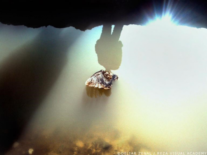Hình bóng phản chiếu của một người tị nạn trong vũng nước tràn ngập ánh mặt trời. (Nguồn: nationalgeographic.com)
