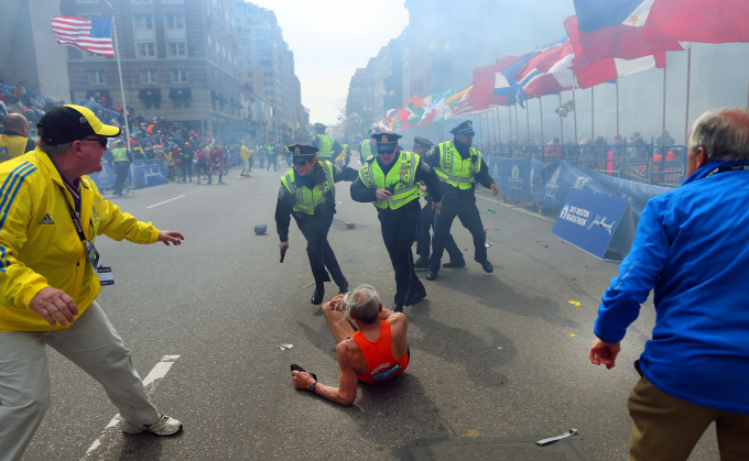 Các sĩ quan cảnh sát đứng cạnh vận động viên marathon Bill Iffrig khi vụ nổ thứ hai vang lên gần vạch đích tại cuộc đua Marathon Boston vào tháng 4-2013. Ba người thiệt mạng và ít nhất 264 người bị thương trong vụ tấn công khủng bố này - Ảnh: Getty Images