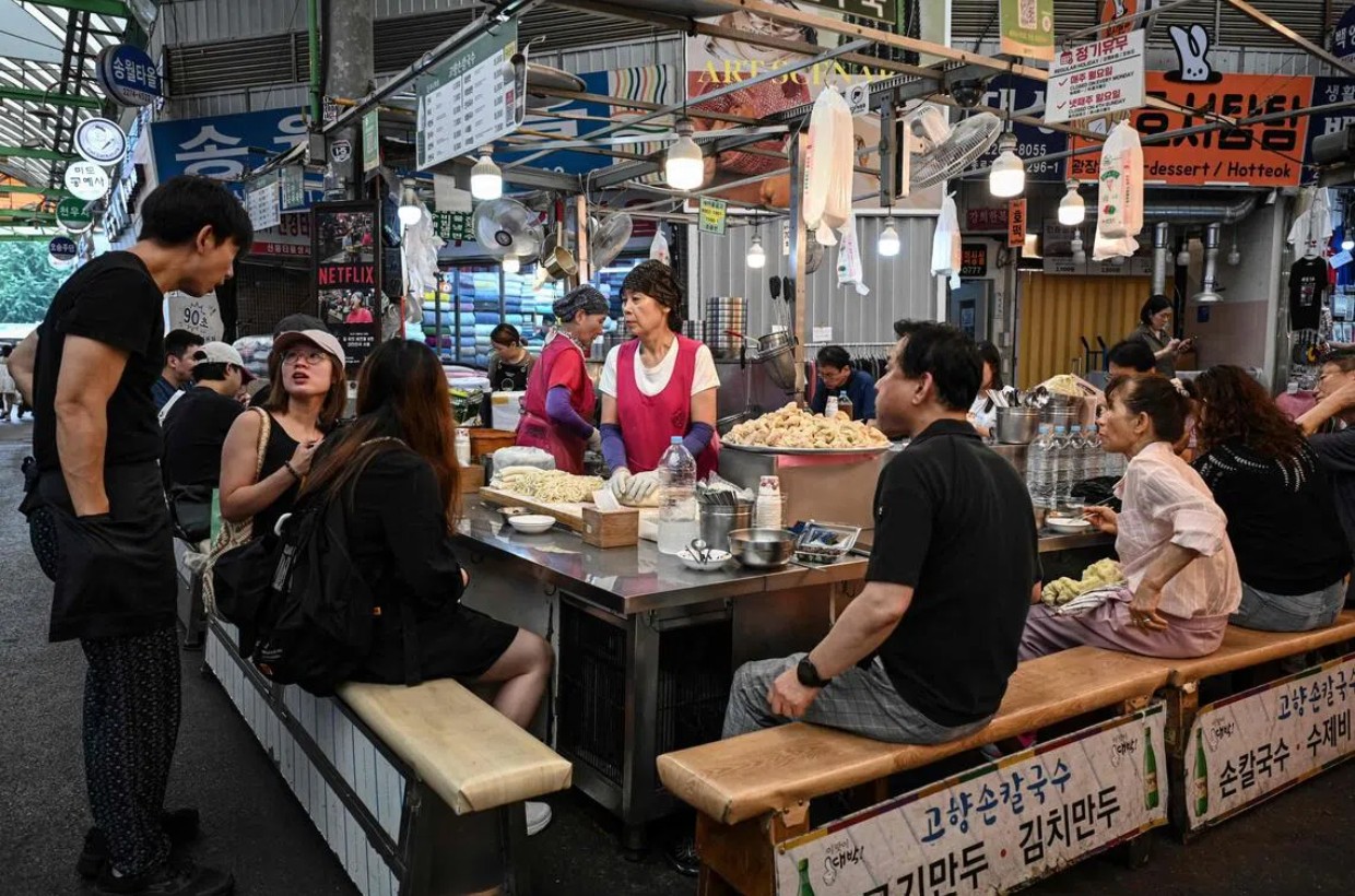 Mọi người dùng bữa tại một quầy bán đồ ăn ở chợ Gwangjang, Seoul - Ảnh: AFP