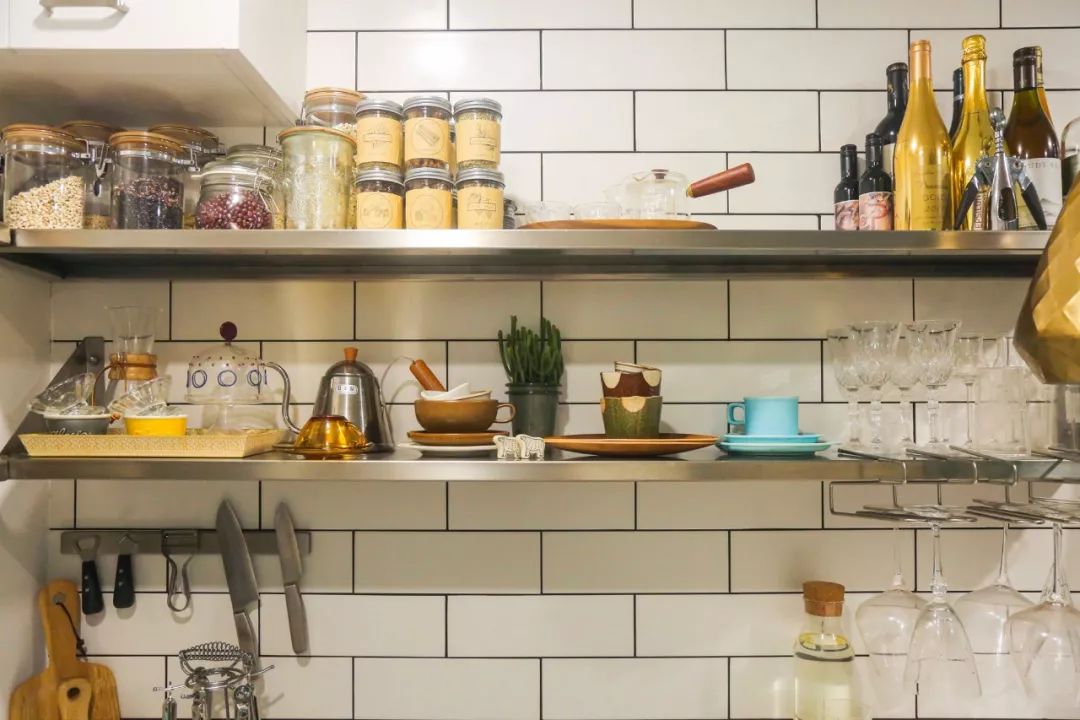   Tường bếp được ốp gạch vuông trắng, thay vì dùng tủ bếp kín, Huang lựa chọn các kệ inox mở. Những bộ bát đĩa, dụng cụ nấu ăn nhiều màu sắc vừa tiện sử dụng, vừa trở thành điểm nhấn trang trí cho căn bếp nhỏ.  