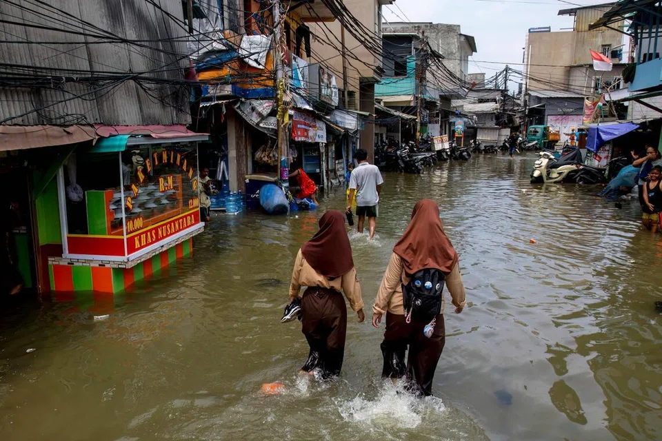 Hai nữ sinh lội qua con phố ngập nước do thủy triều dâng cao ở Muara Baru, Jakarta, ngày 6 tháng 12 năm 2025. ẢNH: AFP