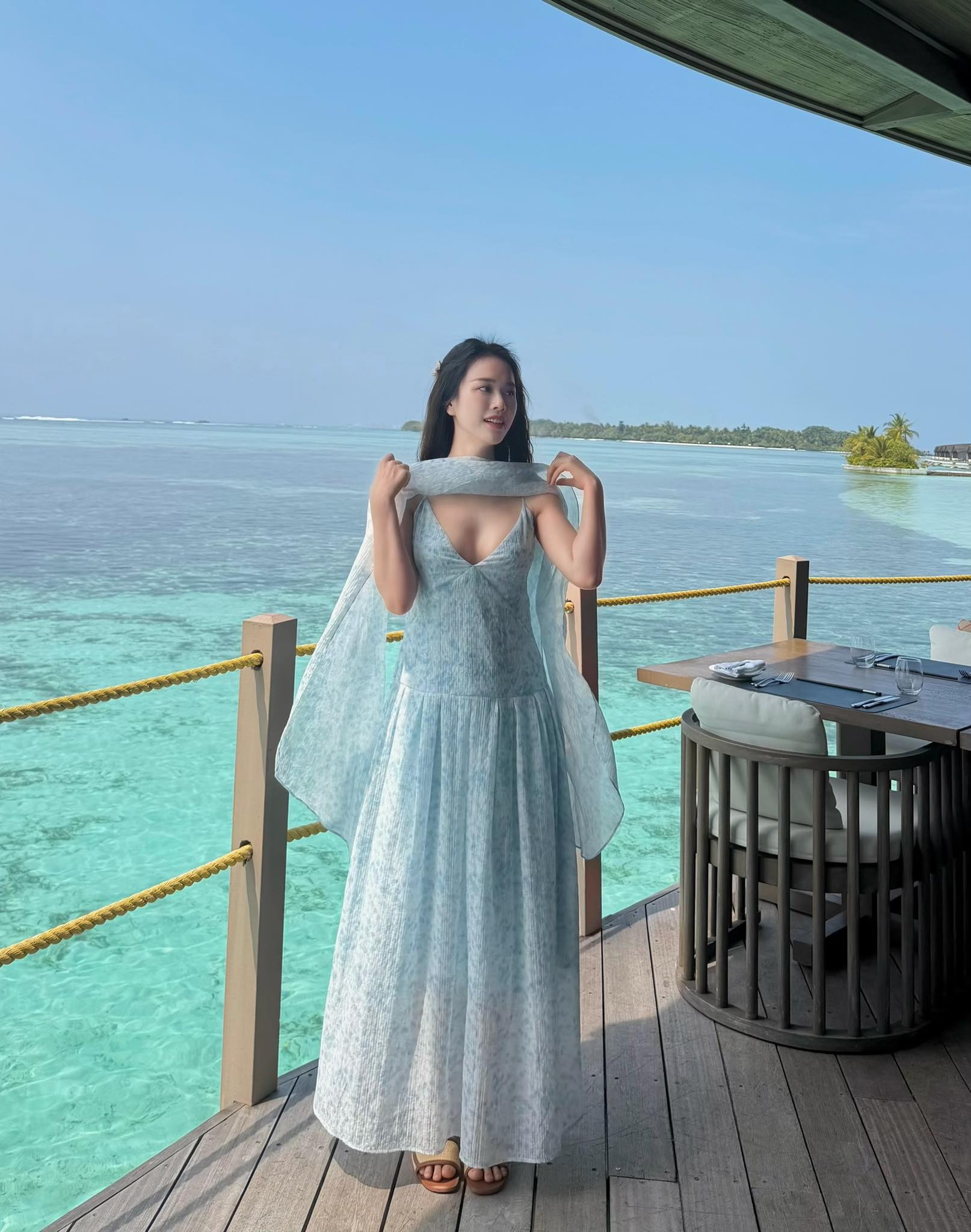 Vi vu đi biển, Mai Phương chọn diện váy dài bay bổng, thướt tha. Dáng váy hai dây màu xanh mướt mắt vừa tôn dáng vừa mang lại cảm giác mát lành, hợp vibe biển. Điểm xuyết thêm chiếc khăn voan mỏng vắt nhẹ qua vai, tổng thể càng thêm mềm mại, nữ tính và cuốn hút.