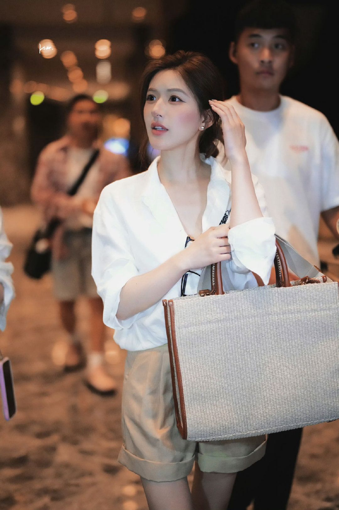 Nếu muốn học cách mặc áo sơ mi trắng theo kiểu nghỉ dưỡng sang chảnh, outfit phối cùng quần short màu be của Triệu Lộ Tư là công thức rất dễ áp dụng. Cô diện sơ mi trắng form rộng vừa phải, sơ vin gọn gàng cùng quần short cạp cao xắn gấu. Phần cổ áo mở nhẹ và tay áo xắn tự nhiên giúp outfit nhìn thoải mái hơn, trong khi túi tote cói viền da nâu lại tăng ngay cảm giác của các chuyến du lịch biển. Đây là bản phối đồ gần như không bao giờ lỗi thời vì vừa trẻ vừa tạo cảm giác sạch sẽ, đắt tiền.