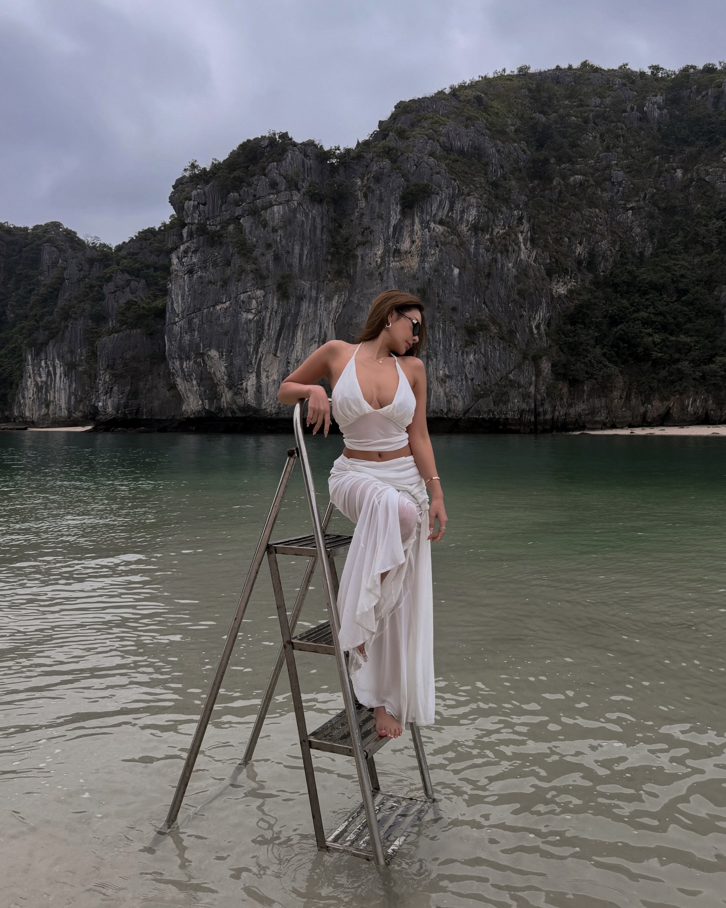 Để tôn lên trọn vẹn nét quyến rũ của Bowlki, set đồ hai mảnh sắc trắng cả nhà AIRÉ STUDIO chính là lựa chọn hoàn hảo cho một chuyến đi biển. Chiếc áo cổ yếm khoét sâu kết hợp ăn ý với chân váy dài xuyên thấu, vừa khéo léo khoe trọn vòng eo con kiến vừa tạo hiệu ứng bay bổng theo từng làn gió. Outift này mang tinh thần phóng khoáng, gợi cảm mà vẫn giữ được nét sang chảnh cực kỳ hút mắt.