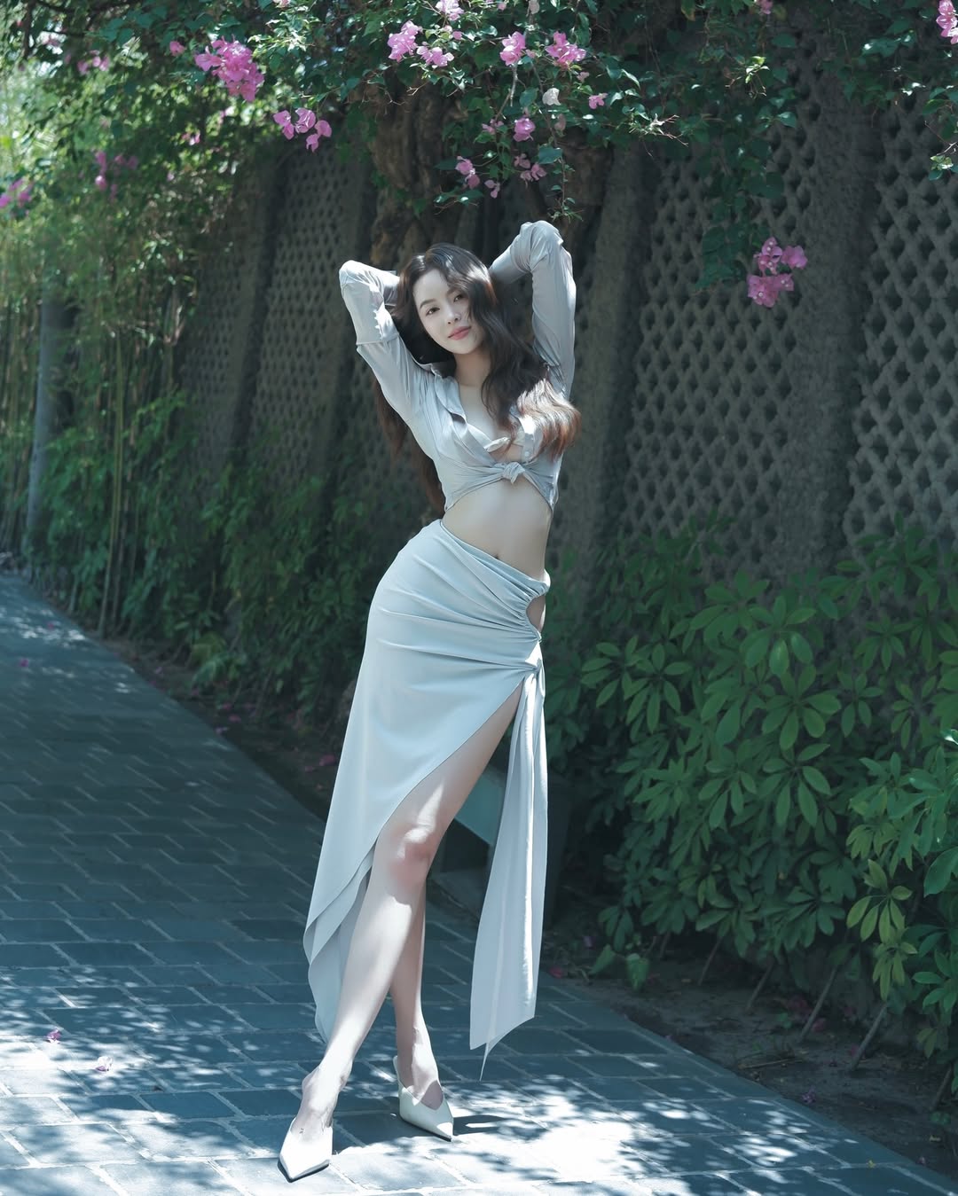 Khi đi biển, Thanh Thủy thiên về style phóng khoáng và quyến rũ khi kết hợp áo sơ mi lụa buộc vạt khoe nội y và chân váy dài xẻ tà. Điểm nhấn cut-out táo bạo ở hông và phần tà bất đối xứng không chỉ ăn gian chiều dài đôi chân mà còn tôn đường cong thắt eo gợi cảm của nàng hậu. Outfit này sẽ là lựa chọn hoàn hảo cho những cô nàng tham dự buổi tiệc tối bên bờ biển hoặc muốn có ảnh nghìn like ở resort sang chảnh.