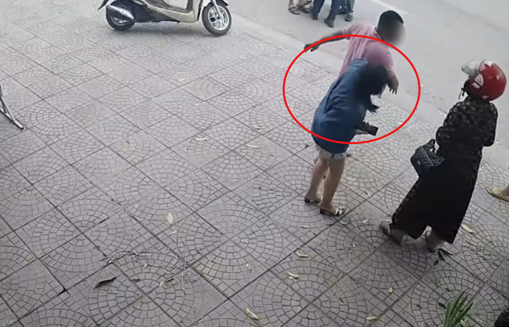Camera ghi lại cảnh người đàn ông dùng tay tác động nhiều lần vào vùng đầu một phụ nữ đứng trên vỉa hè. 