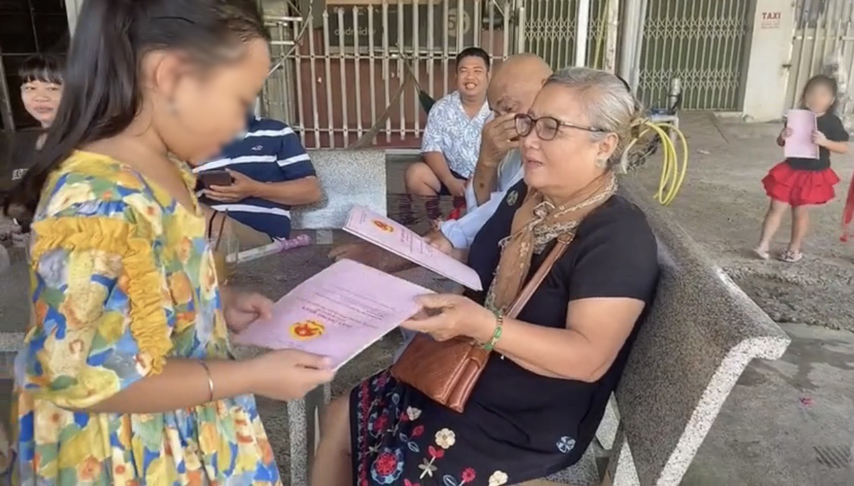 Bà Kiều lần lượt phát từng quyển sổ đỏ cho các cháu nội, ngoại của mình. (Ảnh: Cắt từ clip)