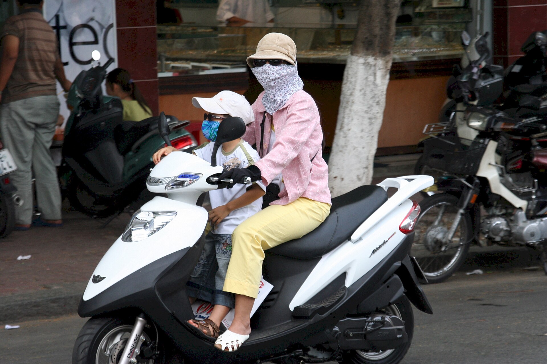 Một người mẹ chở con bằng xe máy tại TP.HCM, ảnh chụp tháng 6/2005. Việc đưa đón người phụ thuộc là một trong những hoạt động có thể định hình chuỗi chuyến đi chăm sóc. Ảnh: Roderick Divilbiss/Wikimedia Commons, CC BY-SA 2.5.
