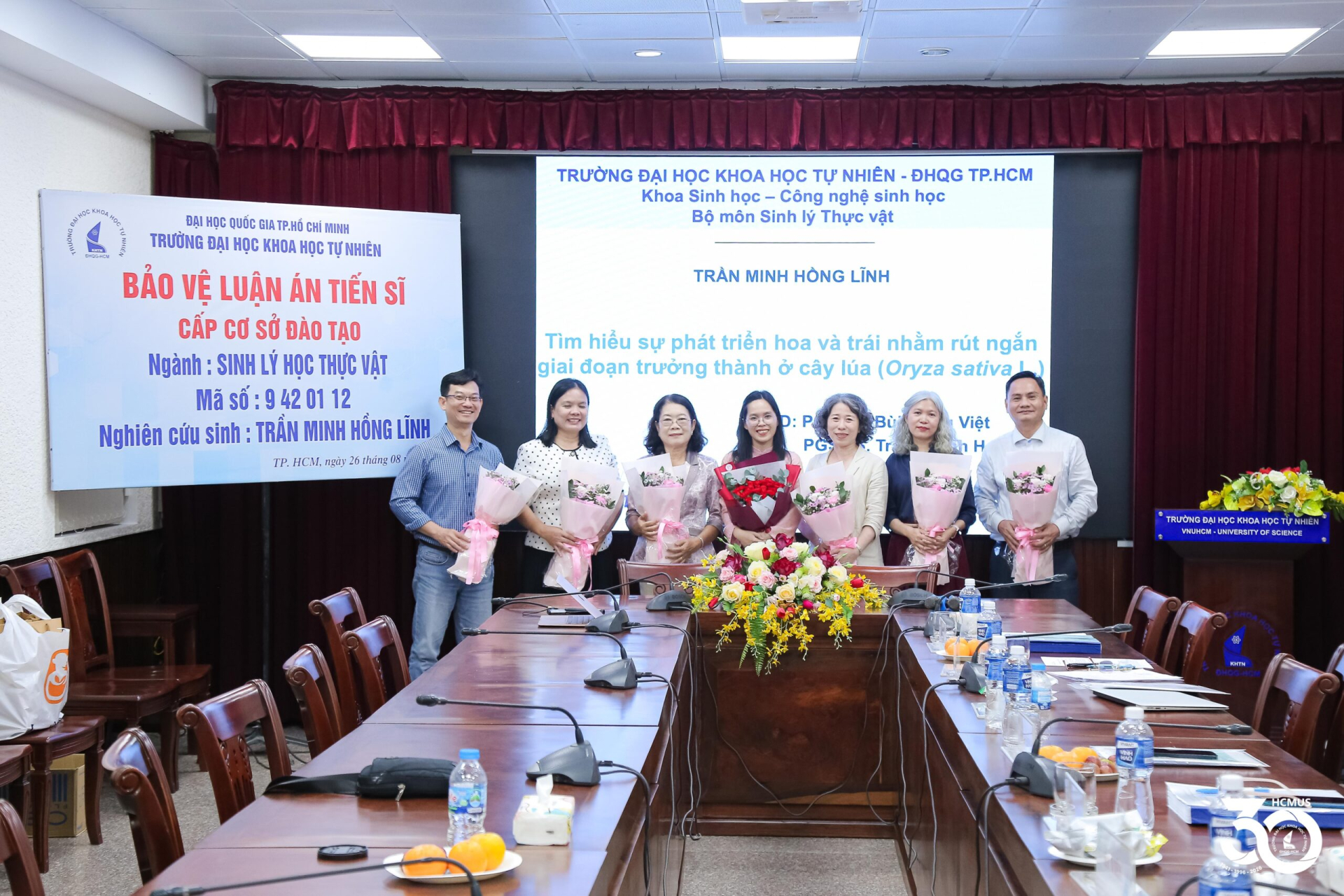 NCS. Trần Minh Hồng Lĩnh cùng người hướng dẫn khoa học và các thành viên Hội đồng sau buổi bảo vệ luận án về rút ngắn giai đoạn trưởng thành ở cây lúa, ngày 26/8/2026. PGS.TS. Trần Thanh Hương là một trong hai người hướng dẫn luận án. Ảnh HCMUS.