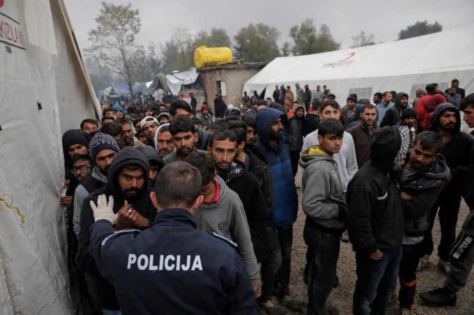 Một cảnh sát Bosian đang cố gắng ổn định hàng dài những người tị nạn đang chờ quần áo và chăn từ thiện ở trại Vucjak/ Ảnh: Reuters