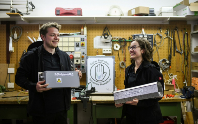 Cô Katharia Obladen (bên phải) và một nhân viên công ty UVIS giới thiệu chiếc hộp khử khuẩn tay vịn thang máy bằng tia UV. Ảnh: AFP.
