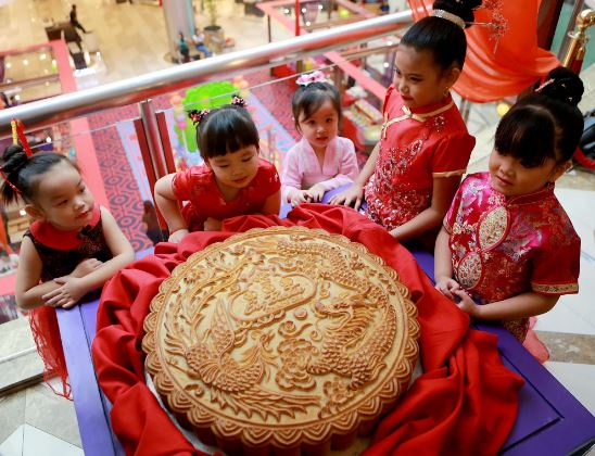 Các em nhỏ đứng xung quanh chiếc bánh trung thu cỡ lớn được trưng bày trong trung tâm thương mại ở Philippines. Ảnh: Xinhua