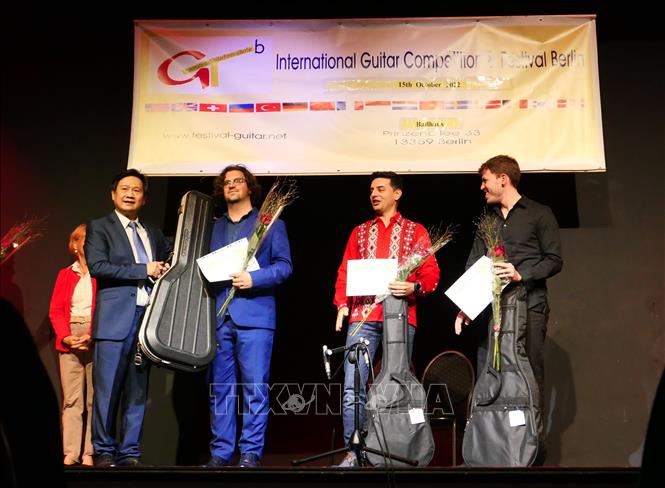 Giáo sư, nhạc sĩ Đặng Ngọc Long (bên trái) trao giải Nhất cho thí sinh đến từ Italy Luca Romanelli, giải Nhì cho thí sinh người Tây Ban Nha Samnuel Beluzan Rodriguez (áo đỏ) và thí sinh giải Ba đến từ Paraguay Raul Rolon. Ảnh: Phương Hoa/PV TTXVN tại Đức