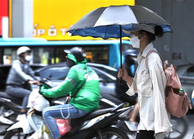   Người dân sử dụng ô, quần áo chống nóng khi phải di chuyển ngoài trời. (Ảnh: Hoàng Hiếu/TTXVN)  