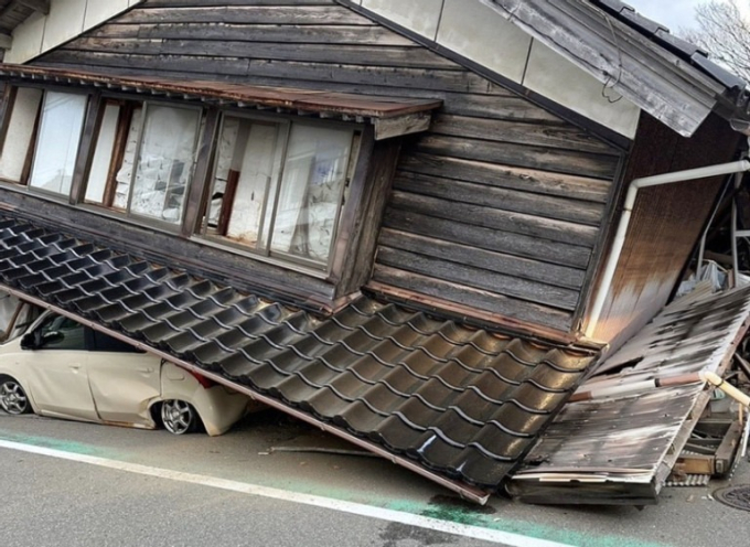 Một căn nhà bị sập, đè nát chiếc xe hơi bên dưới. Ảnh: Kyodo News