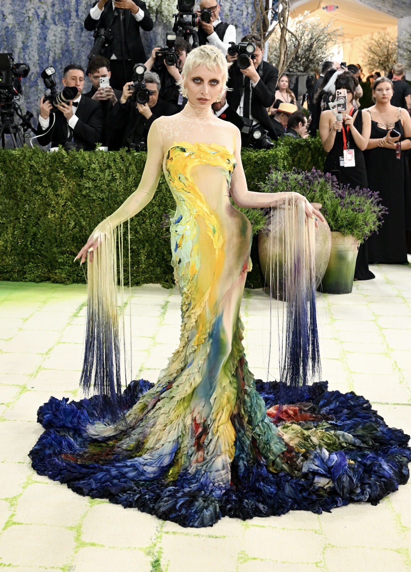   Emma Chamberlain trở lại Met Gala 2026 với vai trò host livestream cho Vogue, là một trong những gương mặt xuất hiện sớm nhất tối nay. Cô mang theo tinh thần của một bảng màu hội họa, diện thiết kế may đo rực rỡ từ Mugler (do Miguel Castro Freitas thực hiện), kết hợp cùng giày Stuart Weitzman.  