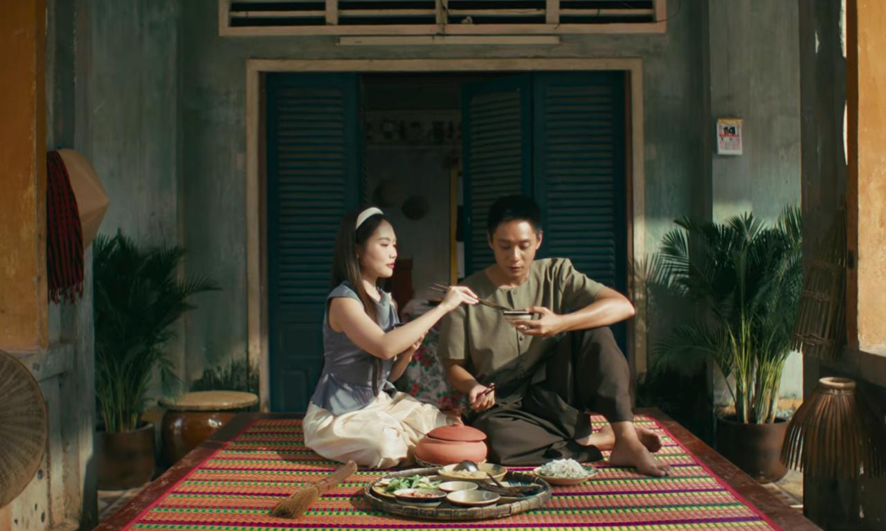 Cảnh Phương Mỹ Chi và bạn trai ngồi trước hiên nhà, cùng thưởng thức món cá kèo mắm me
