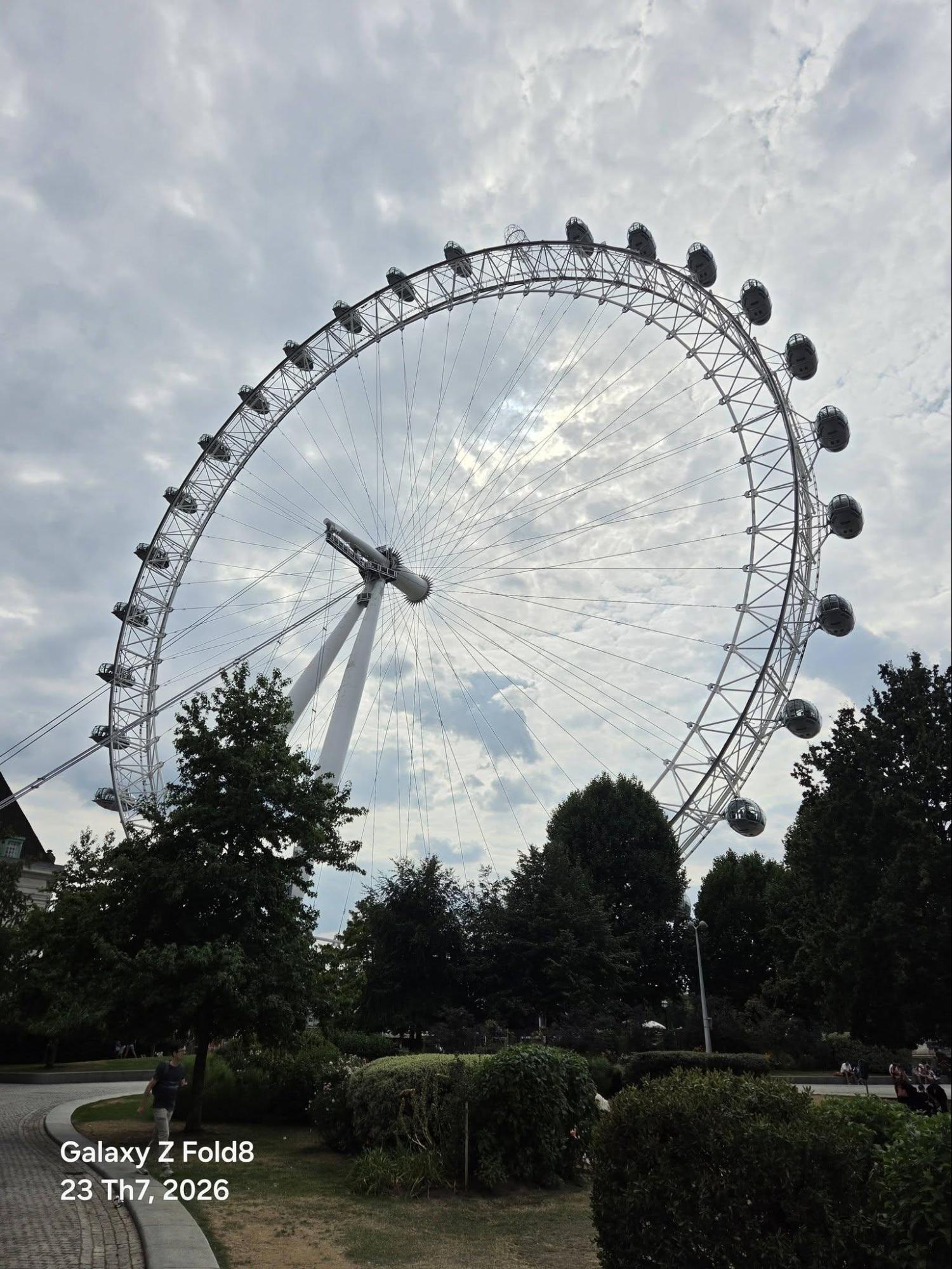 Vòng quay London Eye cao 135m, còn khu vườn phía dưới chỉ cách chân trụ vài chục mét, khoảng cách mà một ống kính tiêu chuẩn sẽ cắt mất phần đỉnh. Ảnh giữ trọn vành bánh xe, giữ luôn hàng cây làm tiền cảnh, và mảng mây phía sau không bị cháy sáng dù máy phải đo sáng cho khung thép tối màu.