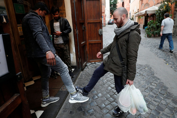 Thay vì ôm hôn, mọi người chào đón nhau bằng chân để tránh tiếp xúc tại Rome (Ảnh: Guglielmo Mangiapane/Reuters).